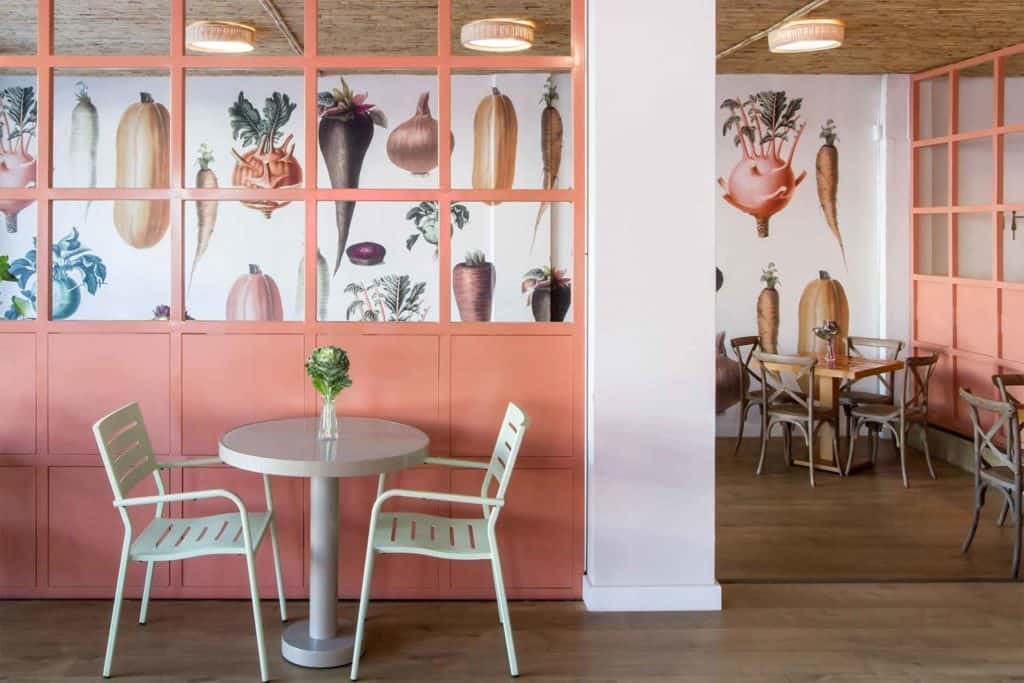 Peach-colored wall panels adorned with vegetable illustrations. The wallpaper features vibrant greens, earthy browns, deep reds, and hints of yellow within the detailed vegetable patterns. Perfect for a cozy cafe ambiance.