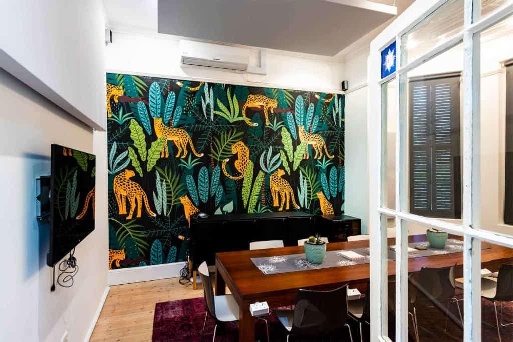 A modern dining room with vibrant jungle-themed wallpaper featuring detailed illustrations of cheetahs and lush tropical plants. The wallpaper design includes vivid greens from various plants, the golden yellow and black spots of cheetahs, along with rich, natural tones interwoven to create a captivating visual experience.