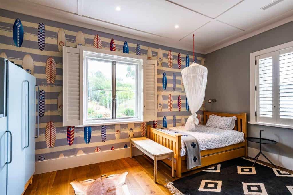 The surfboard-patterned wallpaper features a blend of vibrant elements and colors, including various shades of blue, teal, white, and sandy beige. The surfboards are depicted in different orientations and styles, some with wave patterns or tropical motifs. Its coastal design evokes a breezy, modern feel perfect for adding character to any room.