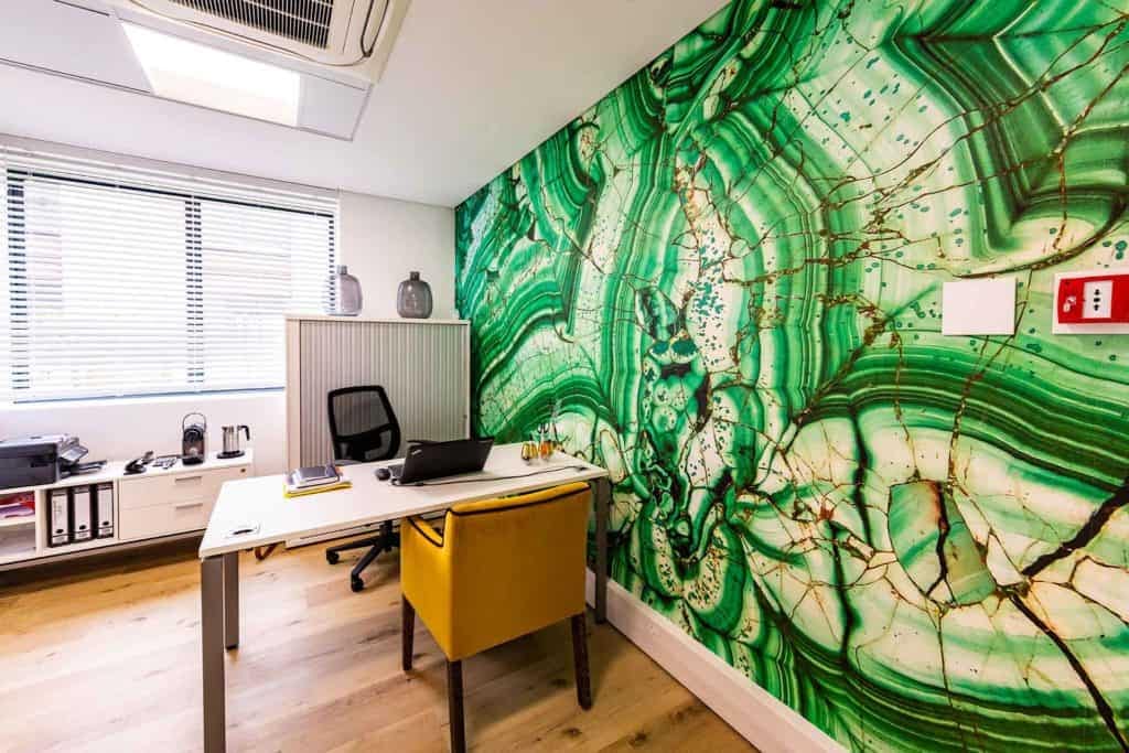 A modern office with a striking **green marble-patterned accent wall**. The wallpaper features varying shades of **emerald, jade**, and hints of **white veining**, creating an elegant, dynamic look. The swirls and patterns evoke a sense of natural stone, adding a sophisticated touch to the room's aesthetic.