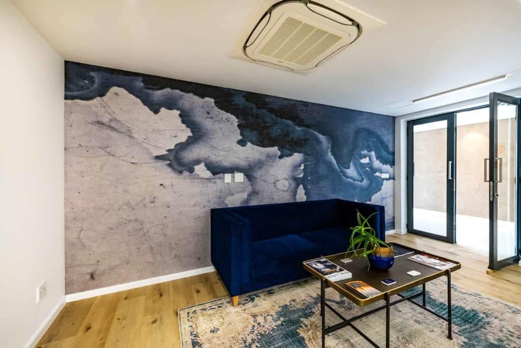 The wallpaper features abstract patterns in shades of blue and grey, resembling the complexity of a financial portfolio. These elements and colors dominate the wall, providing a sophisticated backdrop to the living room.