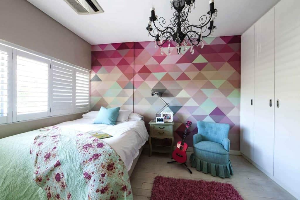 The wall displays a colorful geometric mural featuring bold patterns and vibrant hues, including shades of blue, red, yellow, and green. The shapes are intricately arranged in a modern, eye-catching design that adds artistic flair to the room.