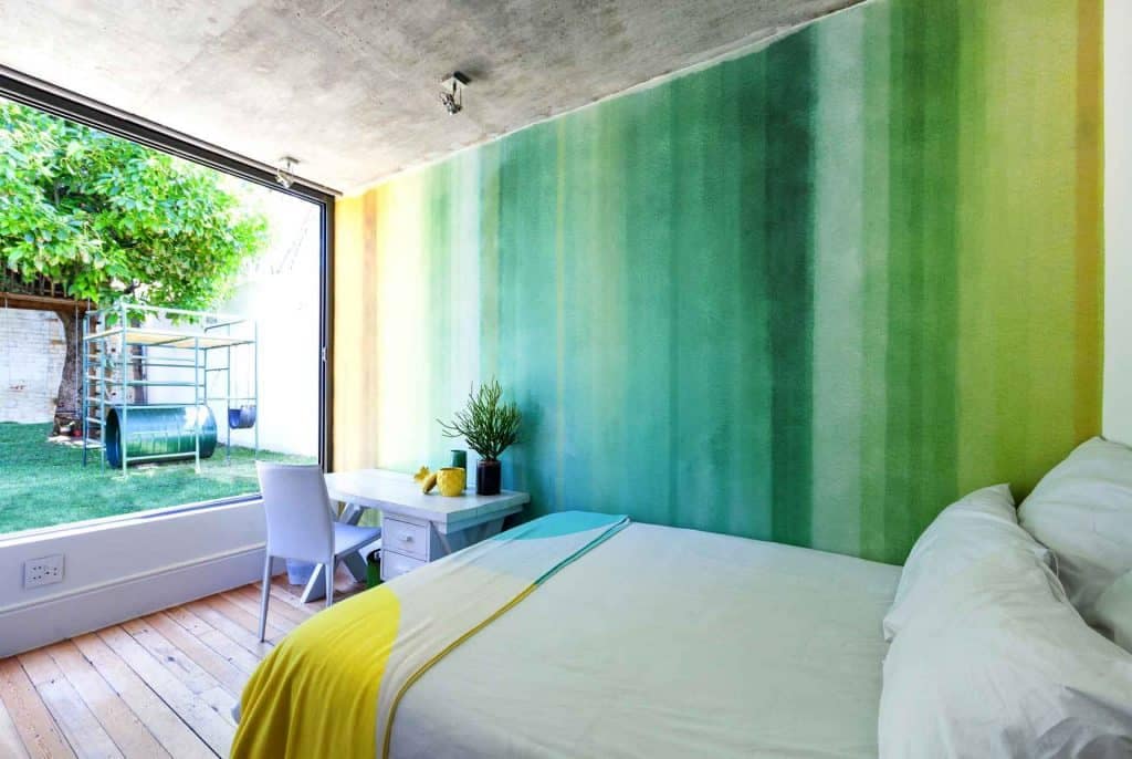 The wallpaper in this modern bedroom features a gradient green design, transitioning from deep emerald at the base to a lighter, serene mint towards the top. Subtle patterns of delicate leaves and abstract flora in various shades of green add texture and sophistication. This stylish wallpaper is perfect for creating a tranquil, nature-inspired ambiance.