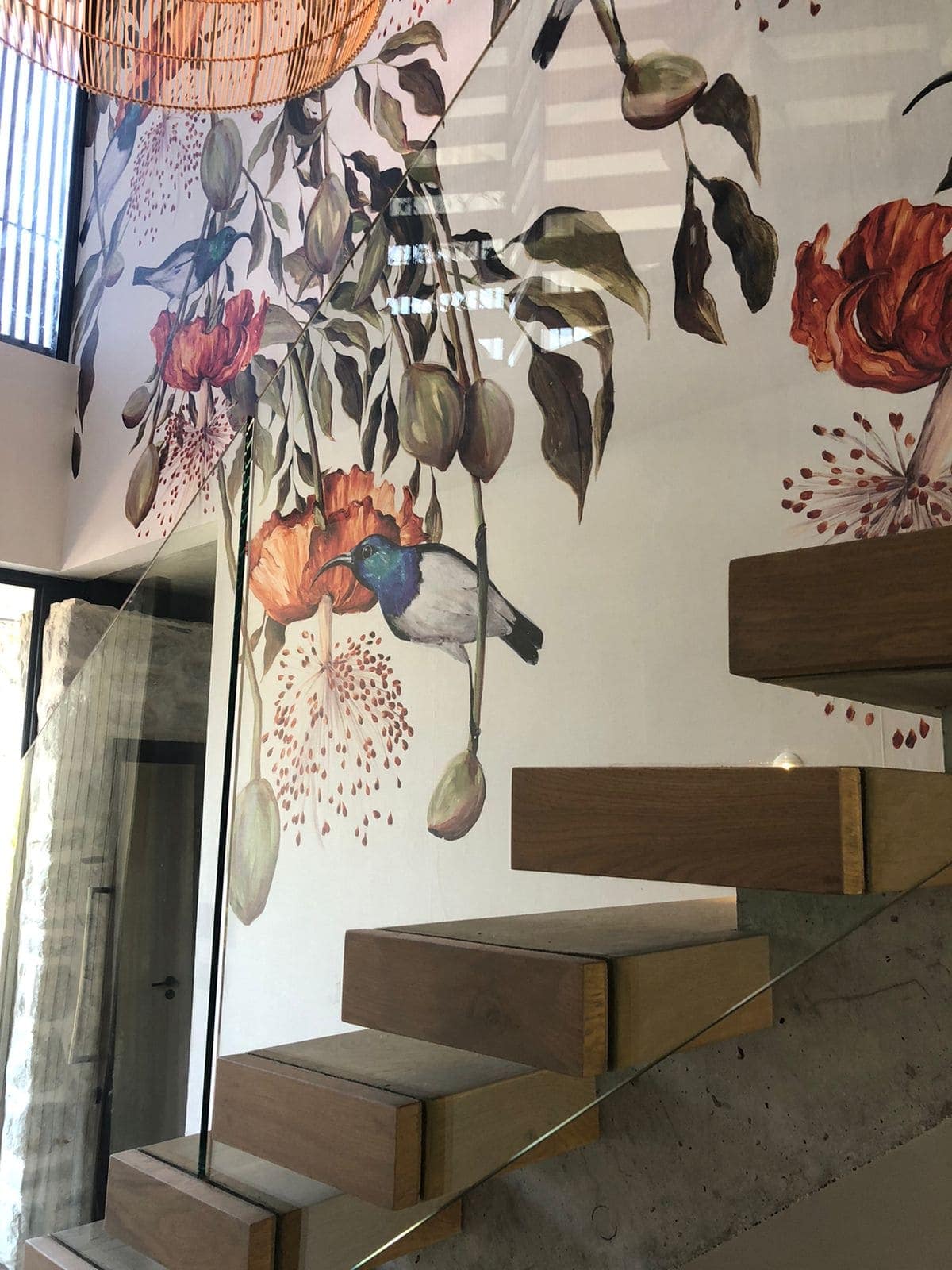Decorative mural on the wallpaper features intricate flowers, leaves, and a colorful bird. Vibrant hues of red, blue, green, and yellow add a dynamic touch.