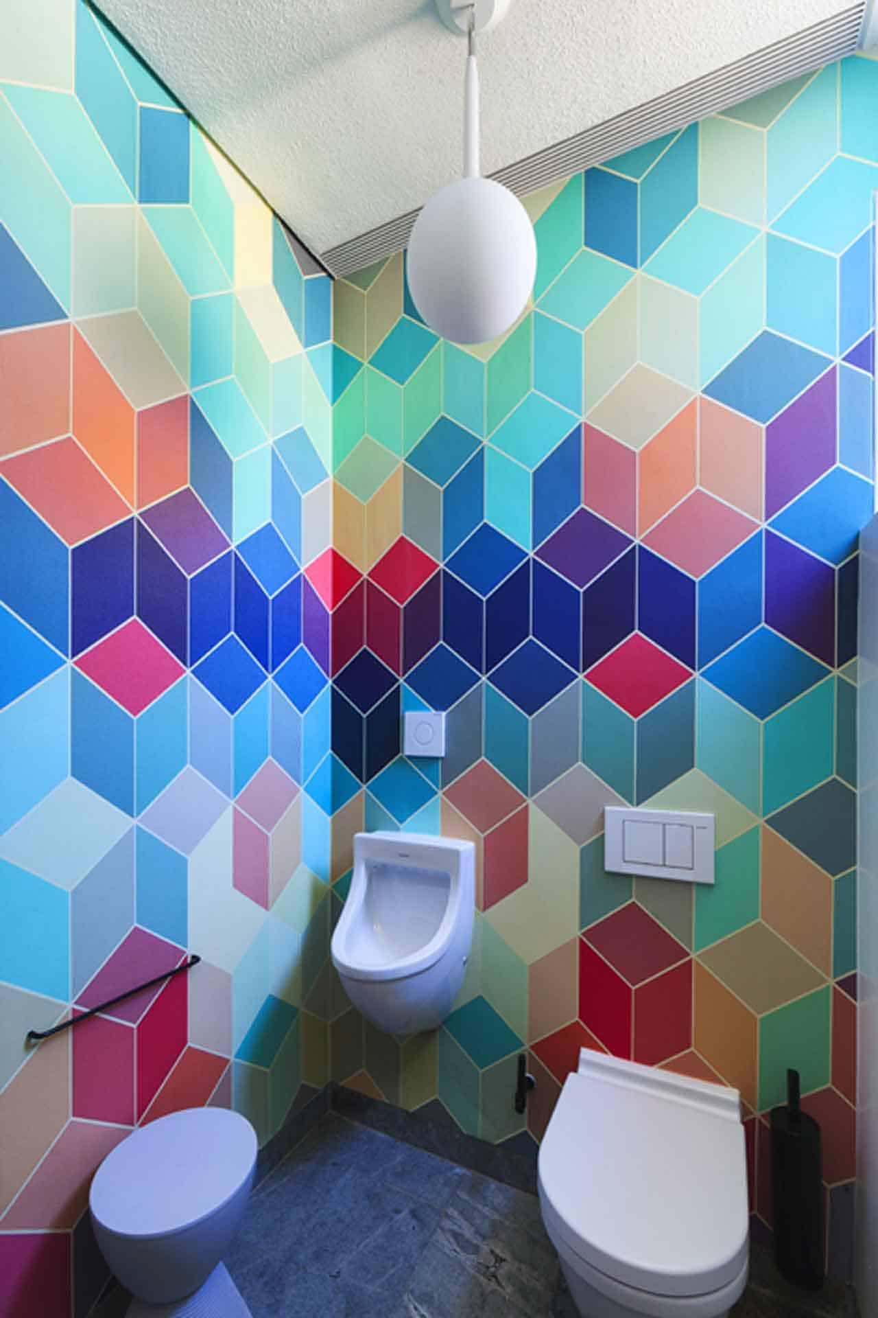 Discover a vibrant restroom adorned with colorful geometric tile patterns creating a visually striking design. The wallpaper boasts shades of blue, red, and green, forming an intricate mosaic that enhances the entire room's modern aesthetic. Perfect for an SEO-friendly portfolio, this eye-catching display combines hues in bold geometric shapes to create an unforgettable ambiance.