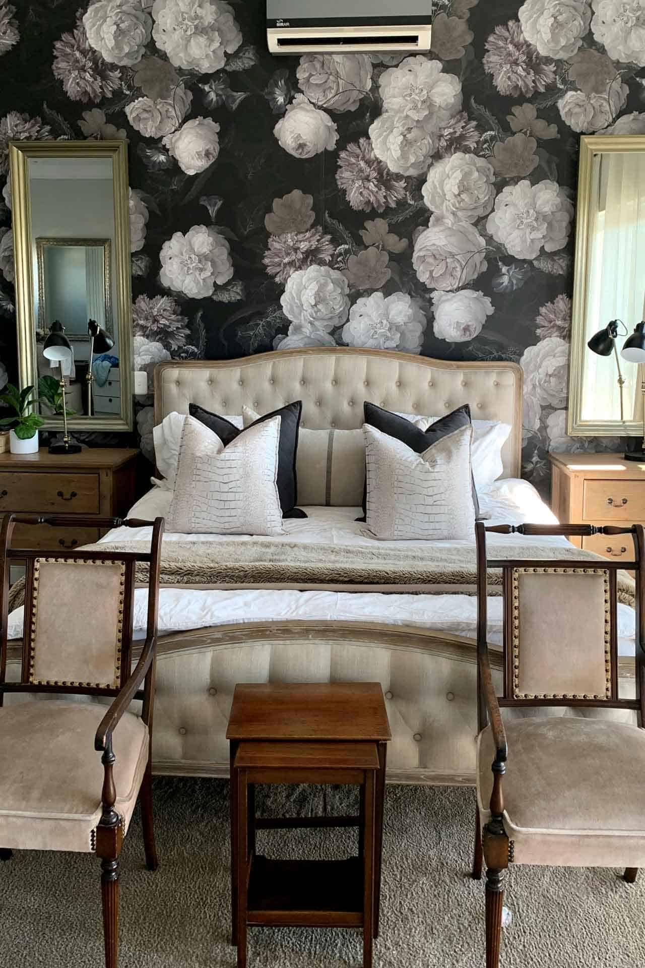 Floral wallpaper backdrop featuring intricate patterns of roses, daisies, and vines in soft pastels—shades of blush pink, lavender, sage green on a cream background.