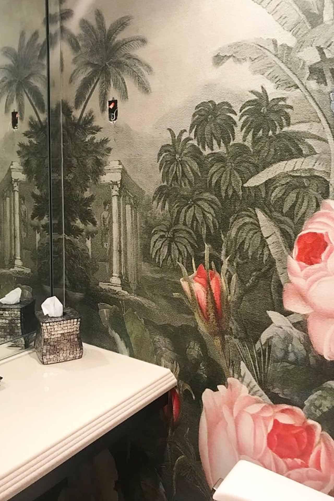 Tropical garden mural wallpaper featuring large pink flowers, lush green foliage, and palm trees. Reflects vibrant colors of pink, green, and earthy tones. Elements include tropical plants and trees for an exotic ambiance.