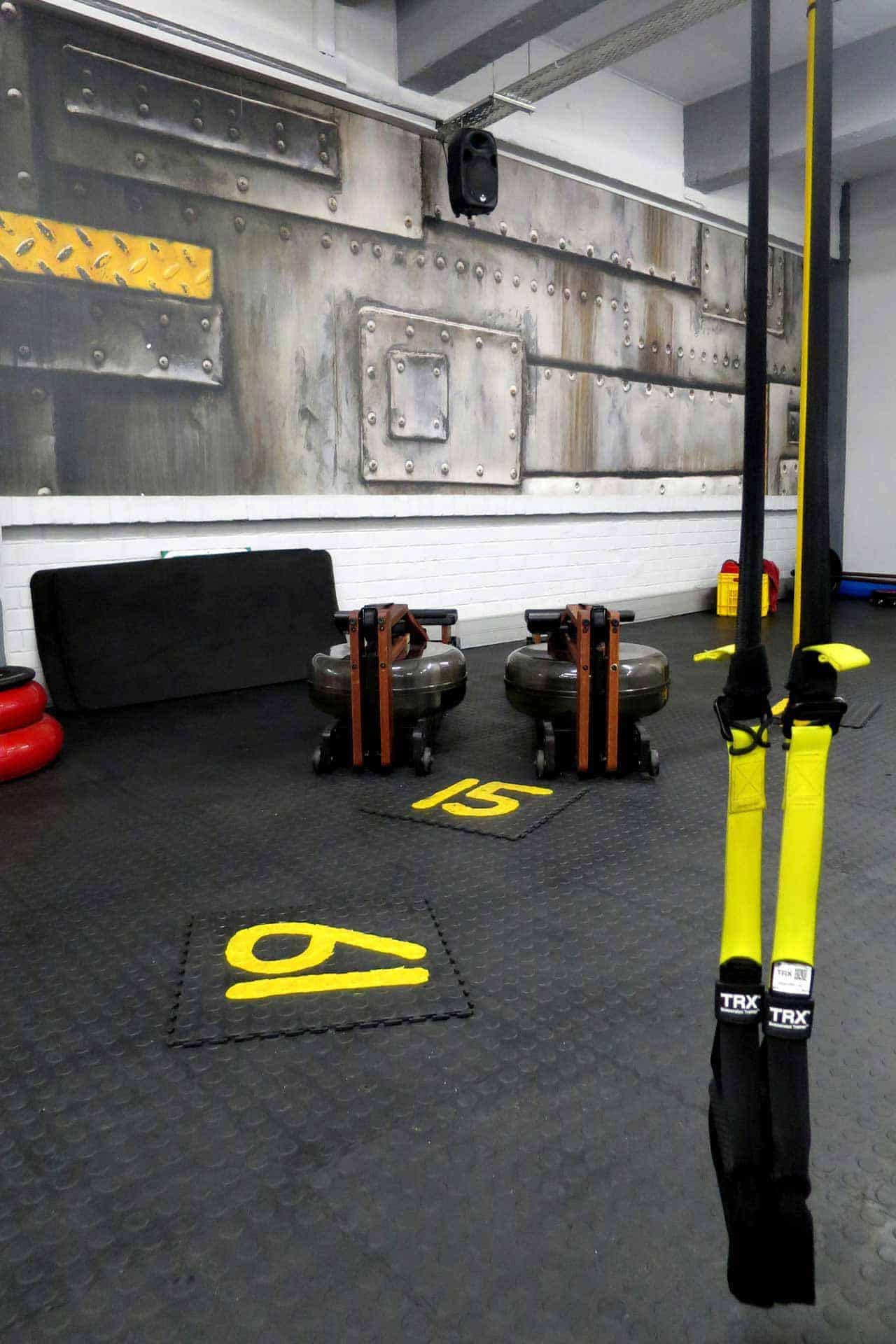 A gym with a gritty, industrial-themed décor features wallpaper adorned with metal panels and rivets, creating a robust ambiance. The wallpaper showcases metallic elements, primarily in shades of gray and silver, adding to the rugged aesthetic.