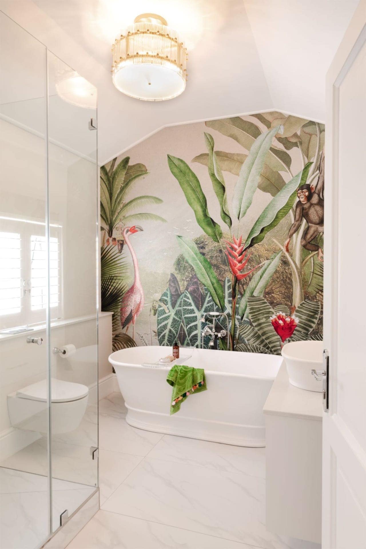 The wallpaper in this tropical-themed bathroom is adorned with lush green foliage, various shades of green leaves, elegant white cranes, and playful brown monkeys. The background integrates subtle earth tones to complement the natural elements. This vibrant design brings an exotic essence to the space.