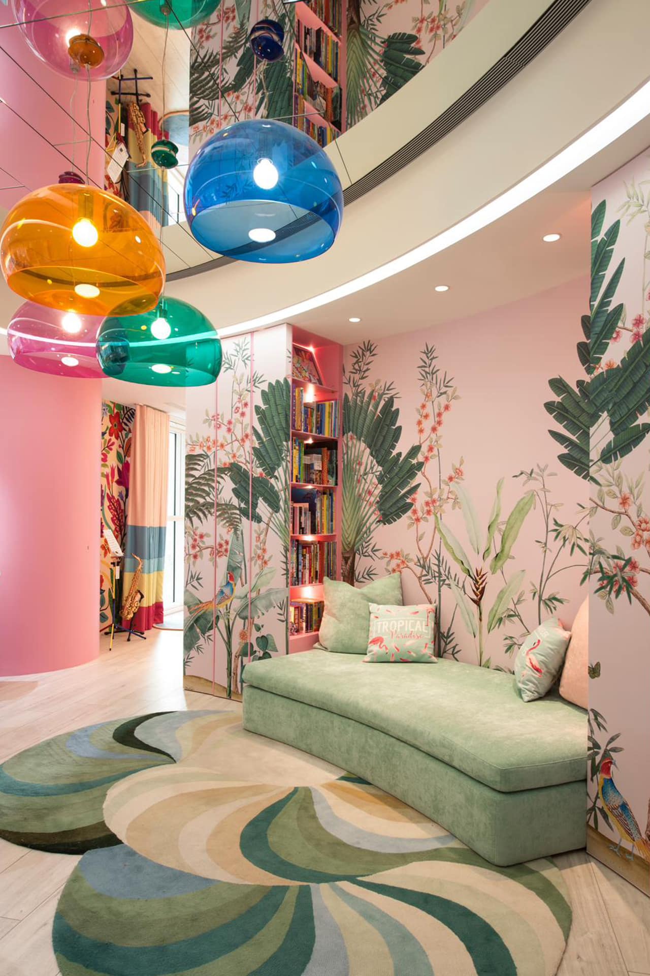 The wallpaper features a vibrant leaf-pattern with shades of green and hints of tropical flora. Colors include deep emerald, lime, and splashes of bright yellow. The design is dense, creating a lush, jungle-like atmosphere that captures the essence of a tropical paradise. Key elements: leaf-patterned wallpaper, green shades, tropical flora.