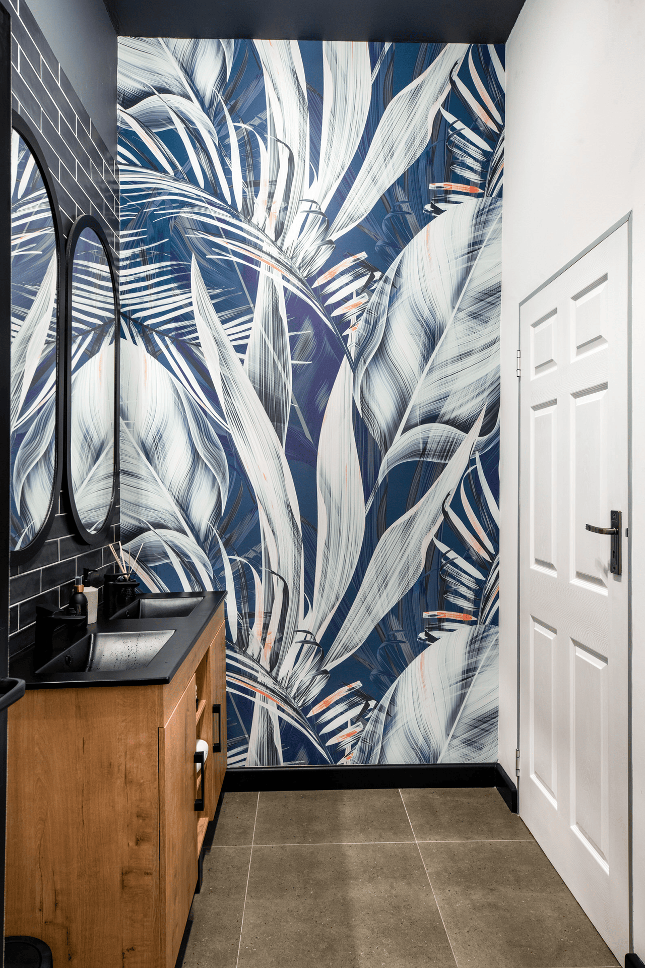 The wallpaper in this modern bathroom is adorned with vibrant, large-scale leaf patterns in striking shades of blue and white. The leaves feature intricate details, blending various hues of blue that range from deep navy to soft sky-blue. The bold design creates a stunning visual contrast against the neutral gray floor tiles, adding a lively and fresh atmosphere to the space. This eye-catching wallpaper combines elegance with nature-inspired elements, making it a standout feature in the room's decor.