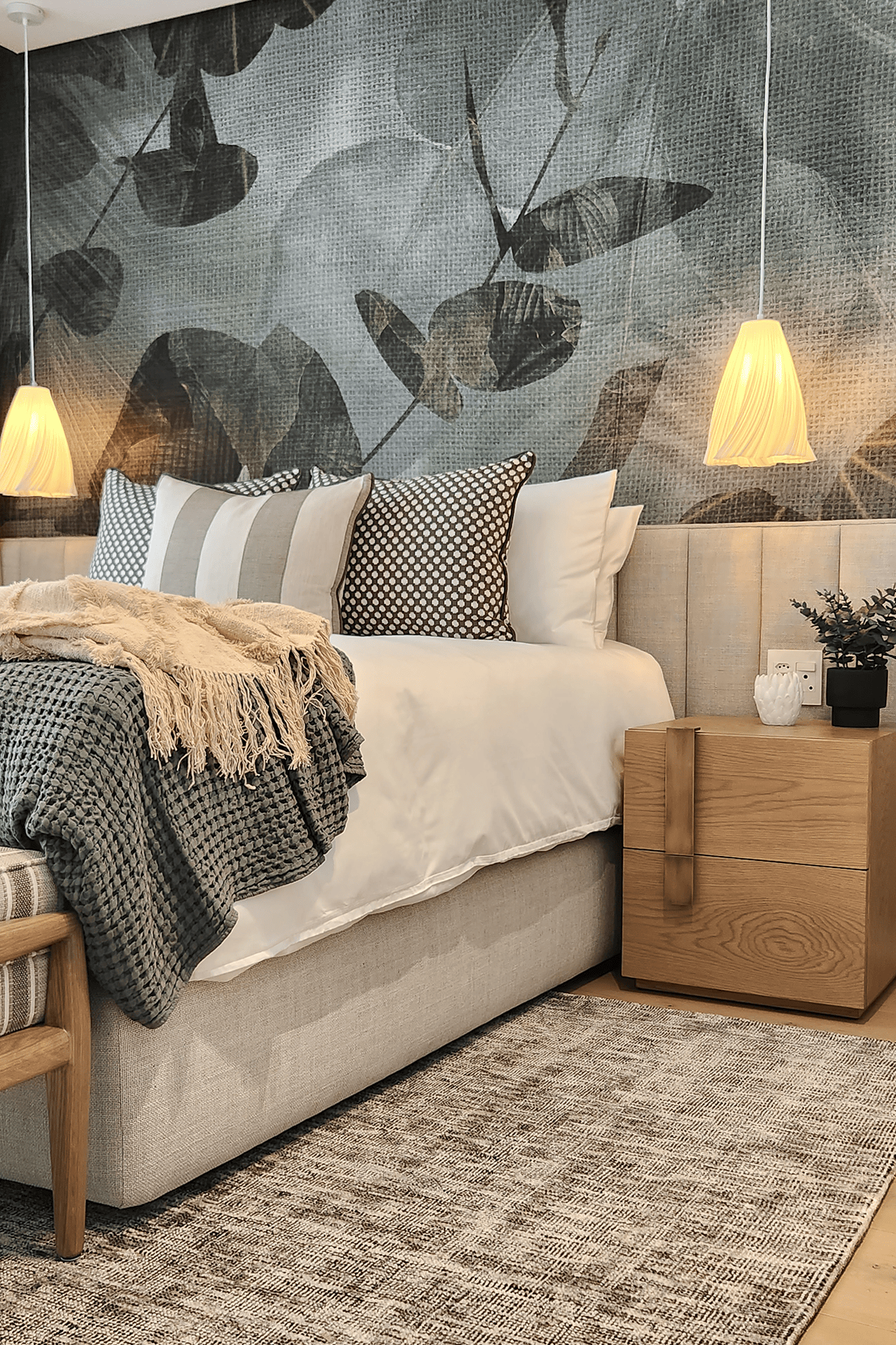 Dark, abstract leaf pattern wallpaper features shades of deep charcoal, muted greys, and subtle hints of black. This intricate design adds a sophisticated touch to the modern bedroom by expertly complementing the room's neutral tones.