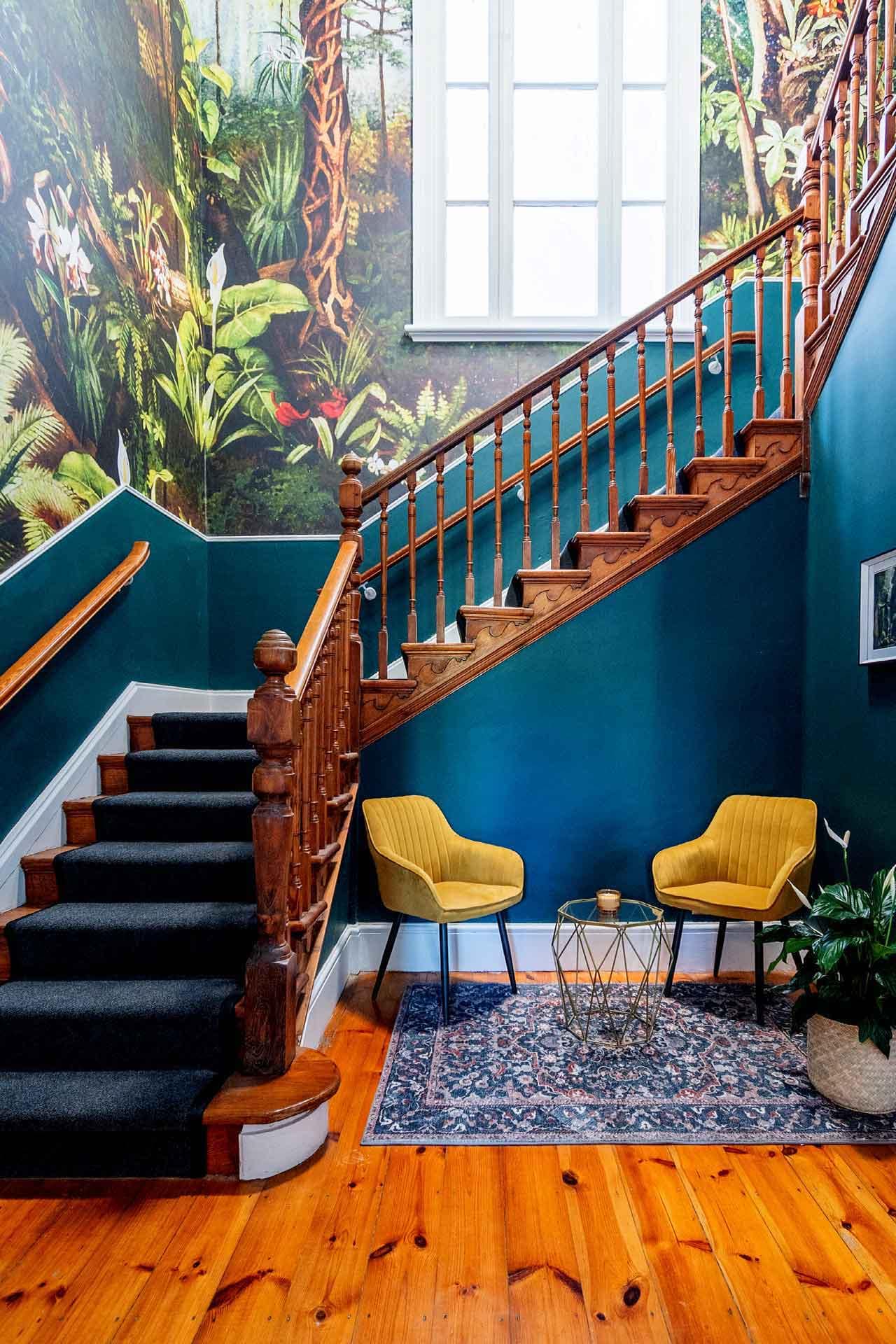 The wallpaper features a lush greenery theme with various shades of green, complemented by intricate floral patterns in vibrant colors. The flowers range from soft pinks and gentle blues to bold reds and yellows, creating a lively and inviting ambiance.