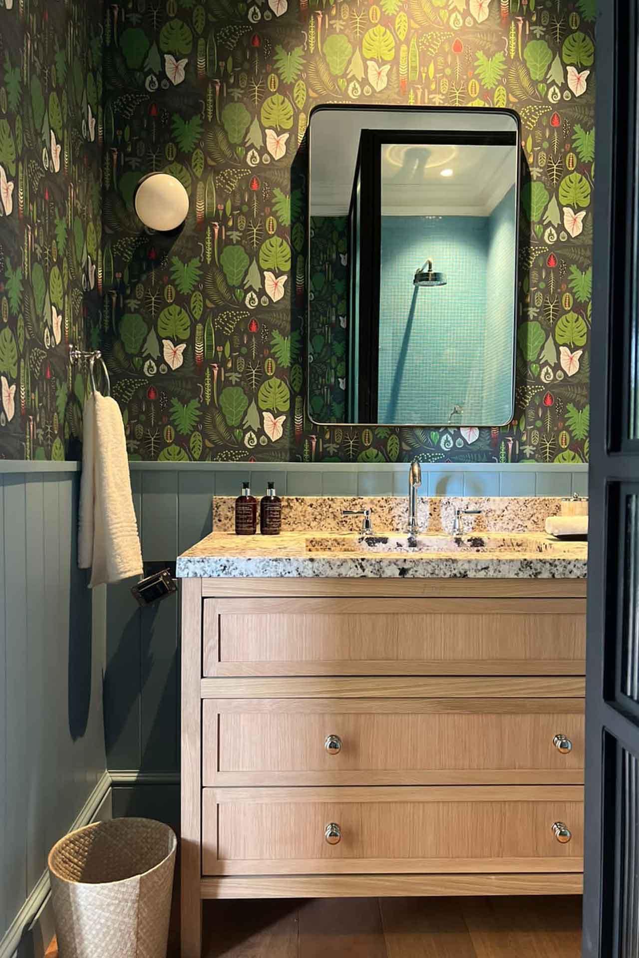 The wallpaper above the sink features lush green foliage patterns, with various shades of rich green leaves against a subtle background. The design incorporates delicate branches and intricate leaf details that create a natural, serene ambiance.