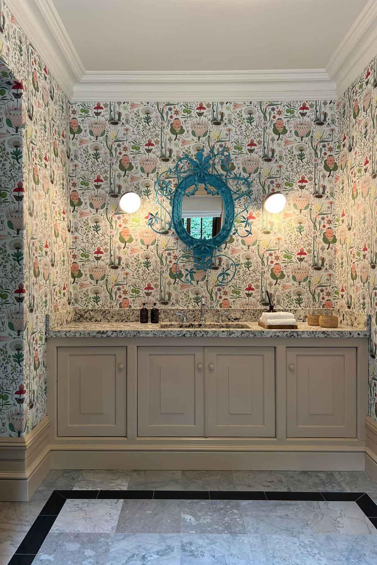 The bathroom features floral wallpaper with vibrant blooms in shades of red, pink, and orange, along with green leaves. The background is a soft cream color interwoven with subtle golden accents enhancing the floral pattern.