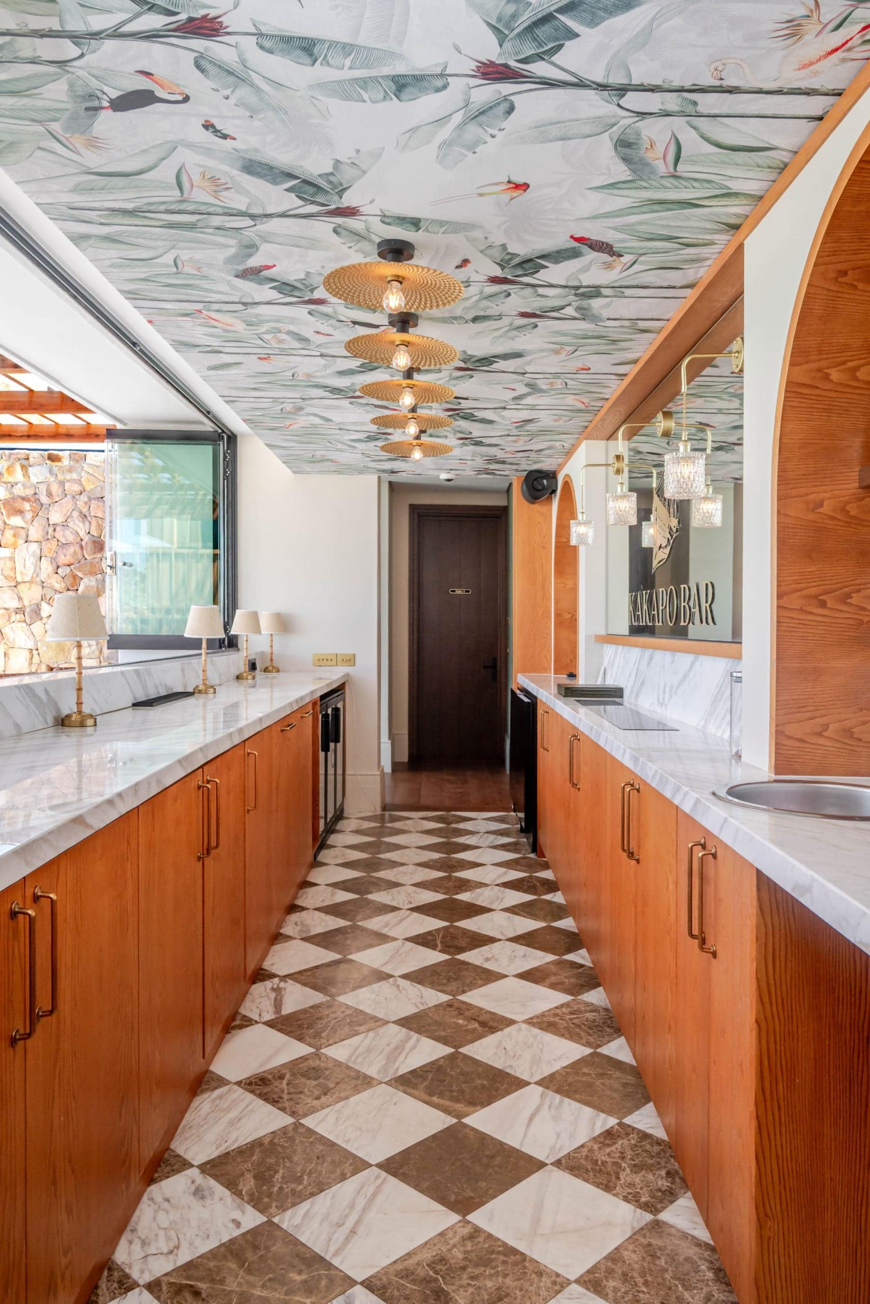 Floral ceiling wallpaper in bold colors creates a dramatic fifth wall effect, with intricate flower patterns and vibrant hues that stand out in the bar area.