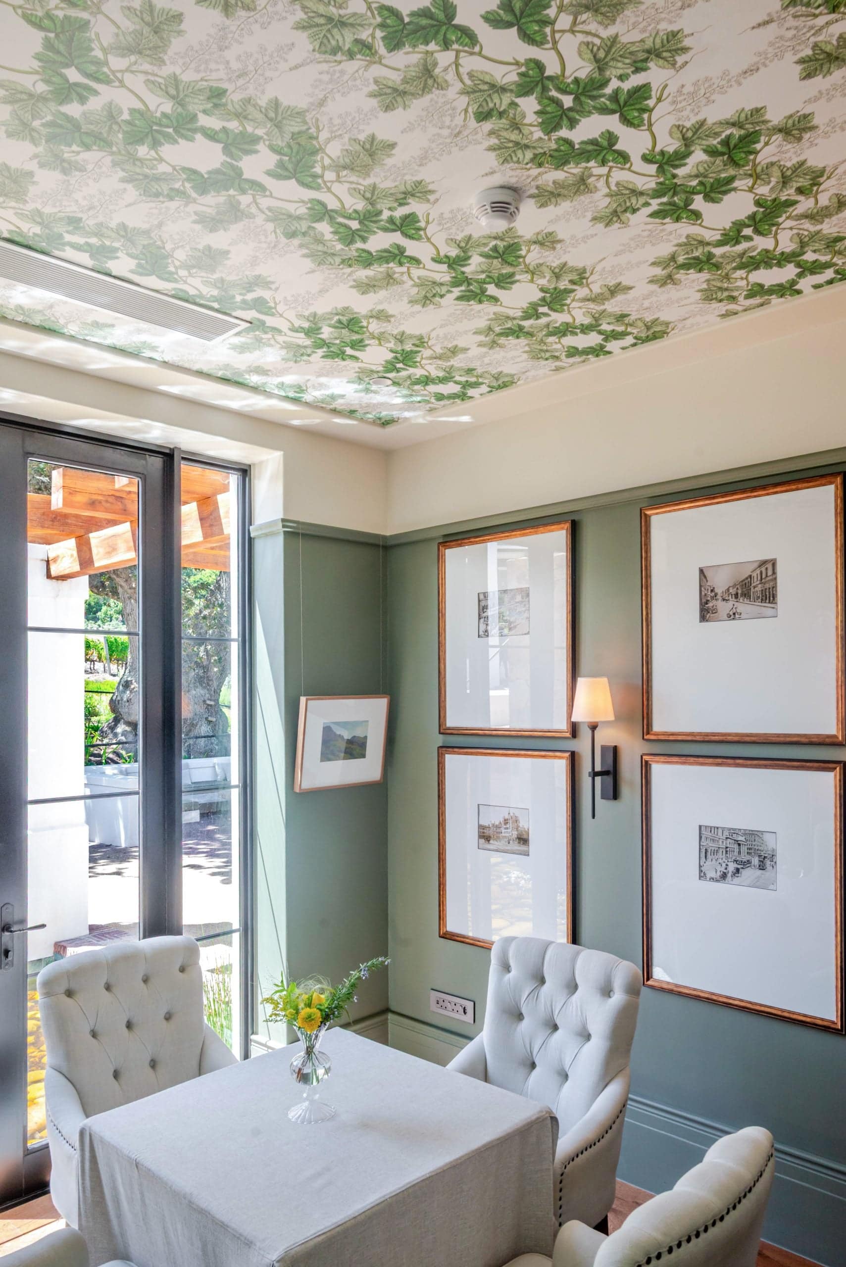 Leafy wallpaper with green botanical patterns decorates the ceiling, creating a nature-inspired fifth wall. The design features assorted leaves in various shades of green, adding a vibrant, organic touch to the room's décor.