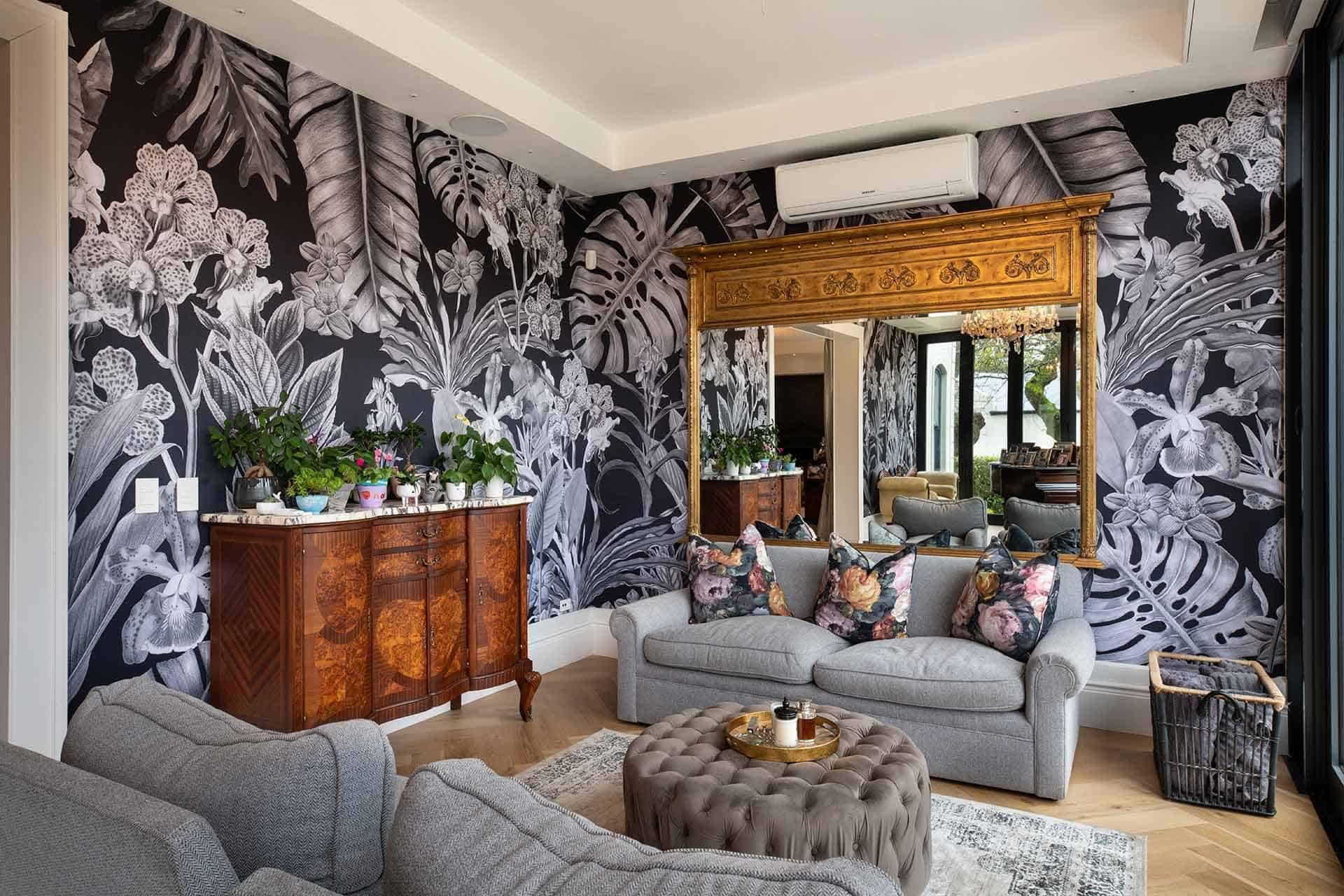 A stylish living room boasts vibrant black and white floral wallpaper. The design is characterized by bold, contrasting flowers and intricate leaf patterns, creating an eye-catching backdrop. The wallpaper features striking shades of black interwoven with crisp white, enhancing the room's sophisticated ambiance. This dynamic design is perfect for adding a touch of elegance to any space.