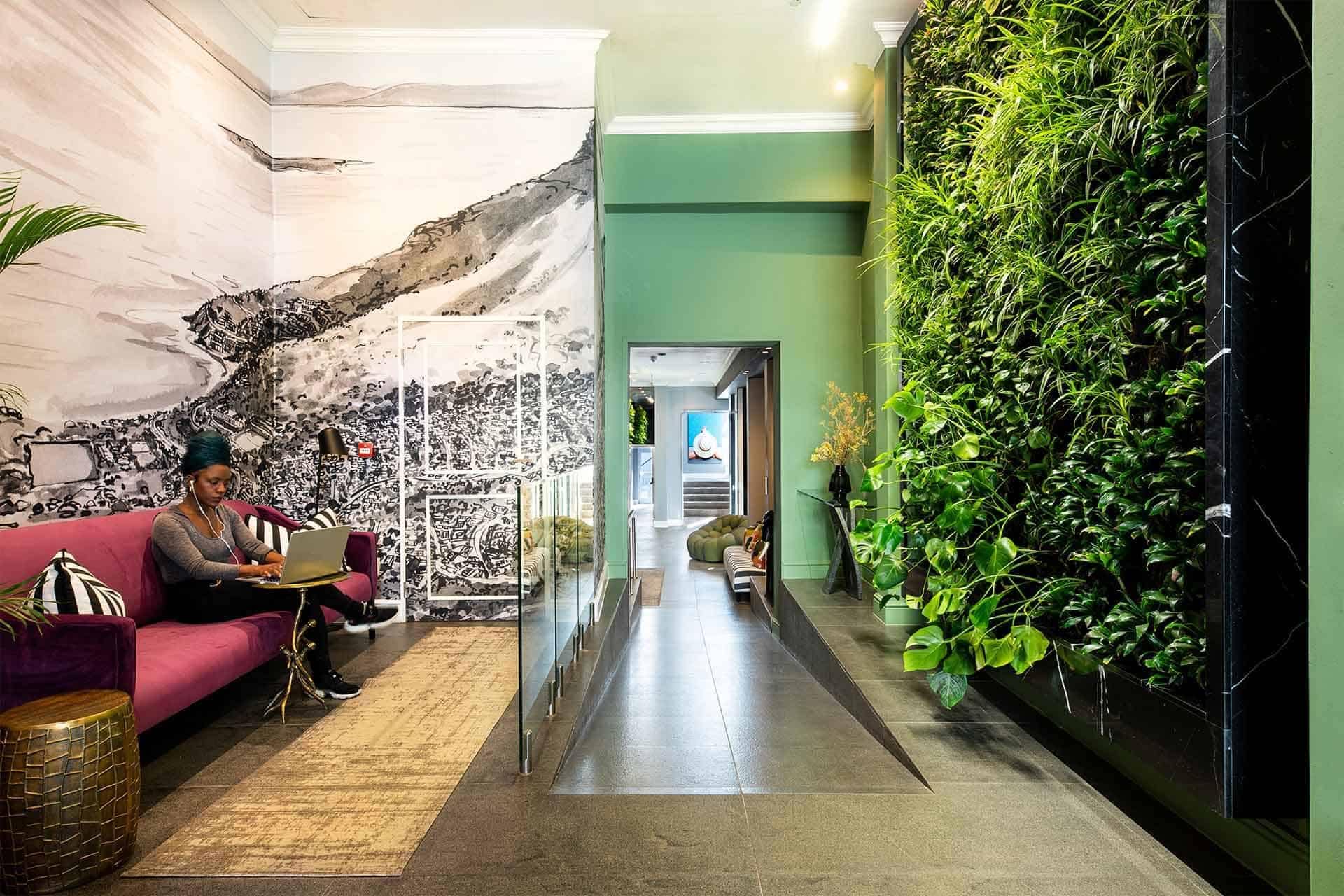 The wallpaper features a vibrant wall mural with abstract geometric shapes and bold colors like teal, mustard yellow, and coral. It blends seamlessly into the stylish decor of the modern office space.