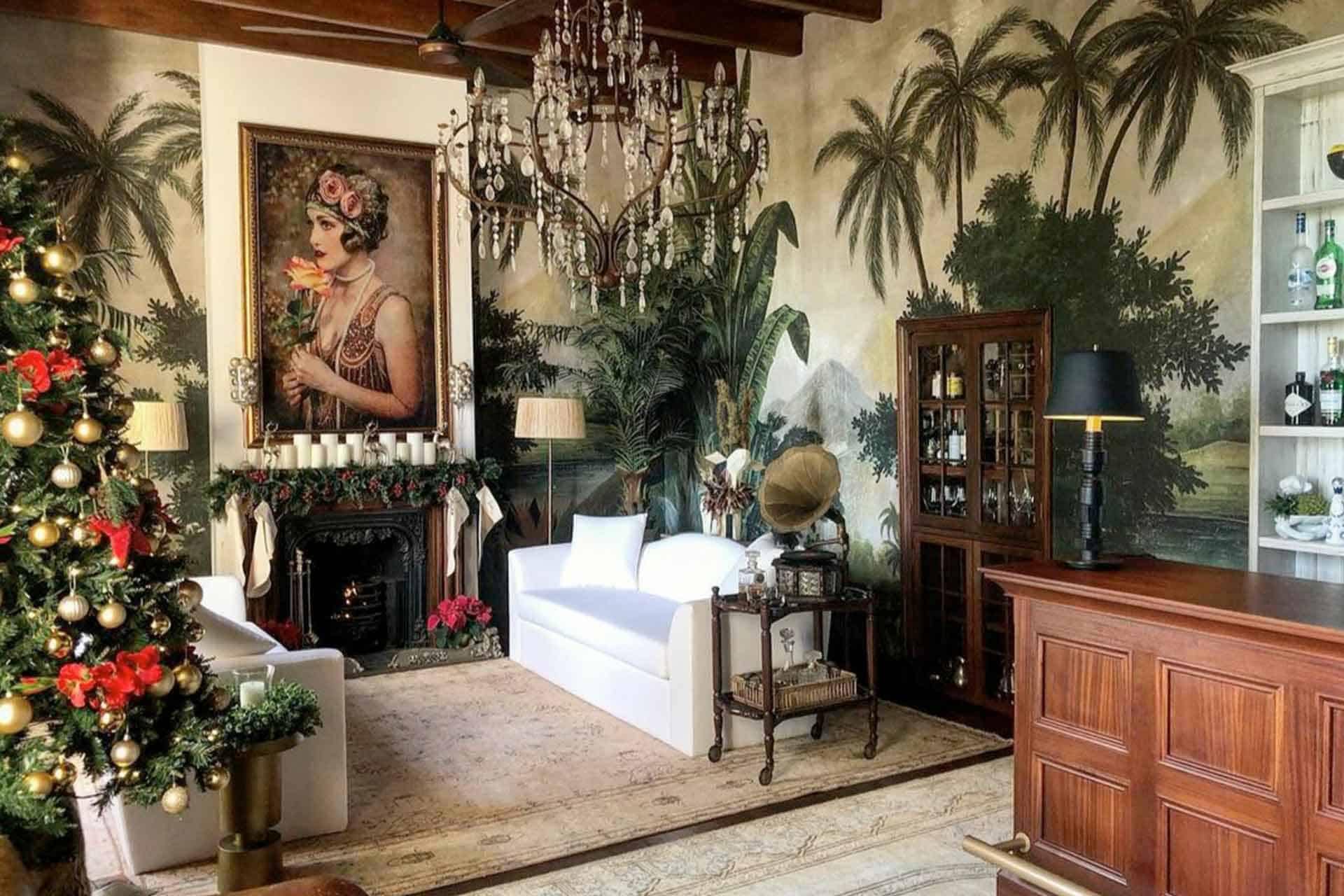 The wallpaper in the luxurious living room features a tropical theme with vibrant colors, including lush greens, deep blues, and exotic floral patterns. It showcases intricate designs of palm leaves and tropical flowers, creating a striking contrast with the elegant furniture and festive decorations. The rich hues and detailed motifs add depth and sophistication to the space while complementing the overall holiday ambiance.