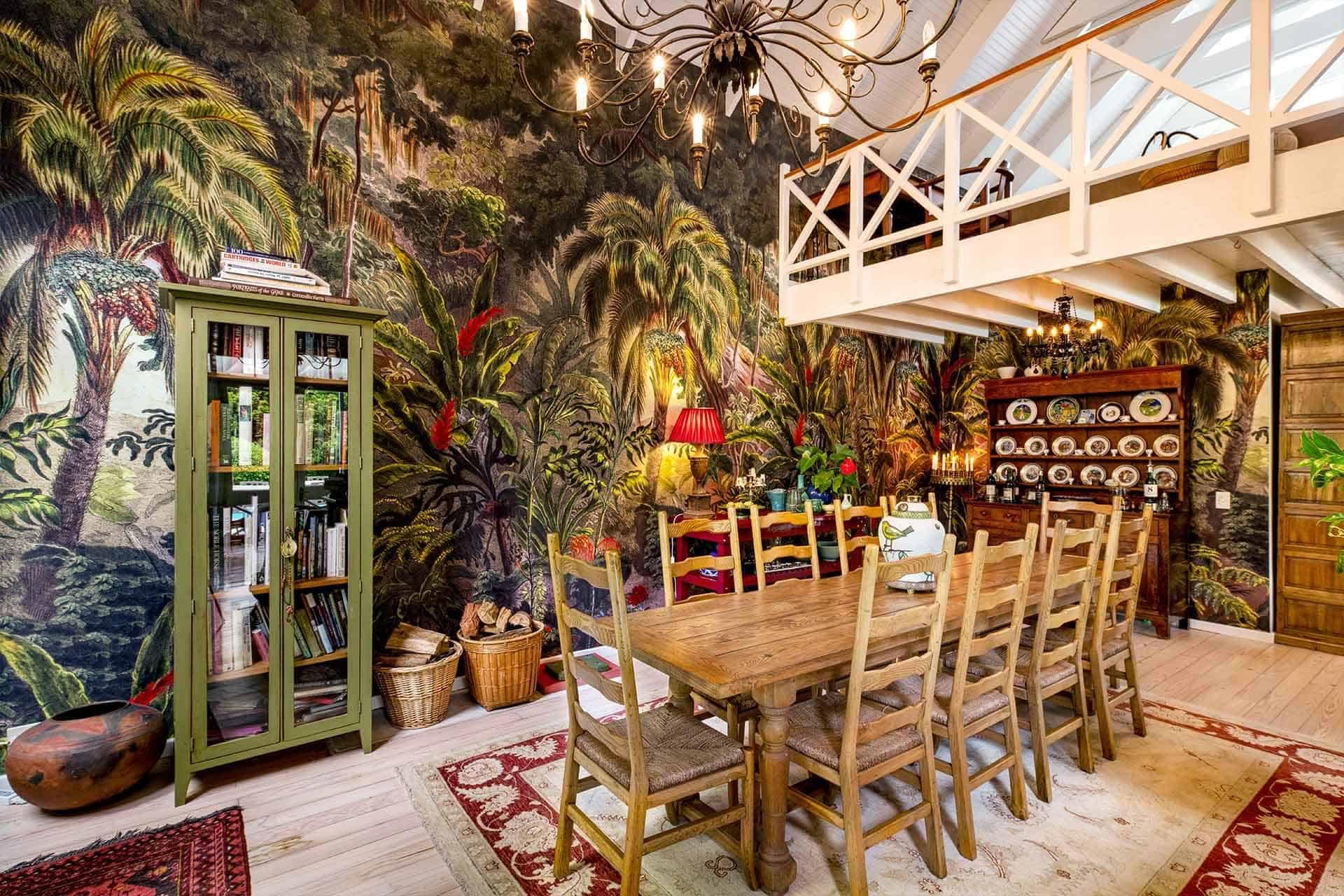 The dining room's walls boast a lush tropical-themed mural, showcasing vibrant green palm fronds, rich blue skies, colorful exotic birds in shades of red and yellow, and bursts of pink hibiscus flowers. These eye-catching elements enhance the room’s eclectic vibe.