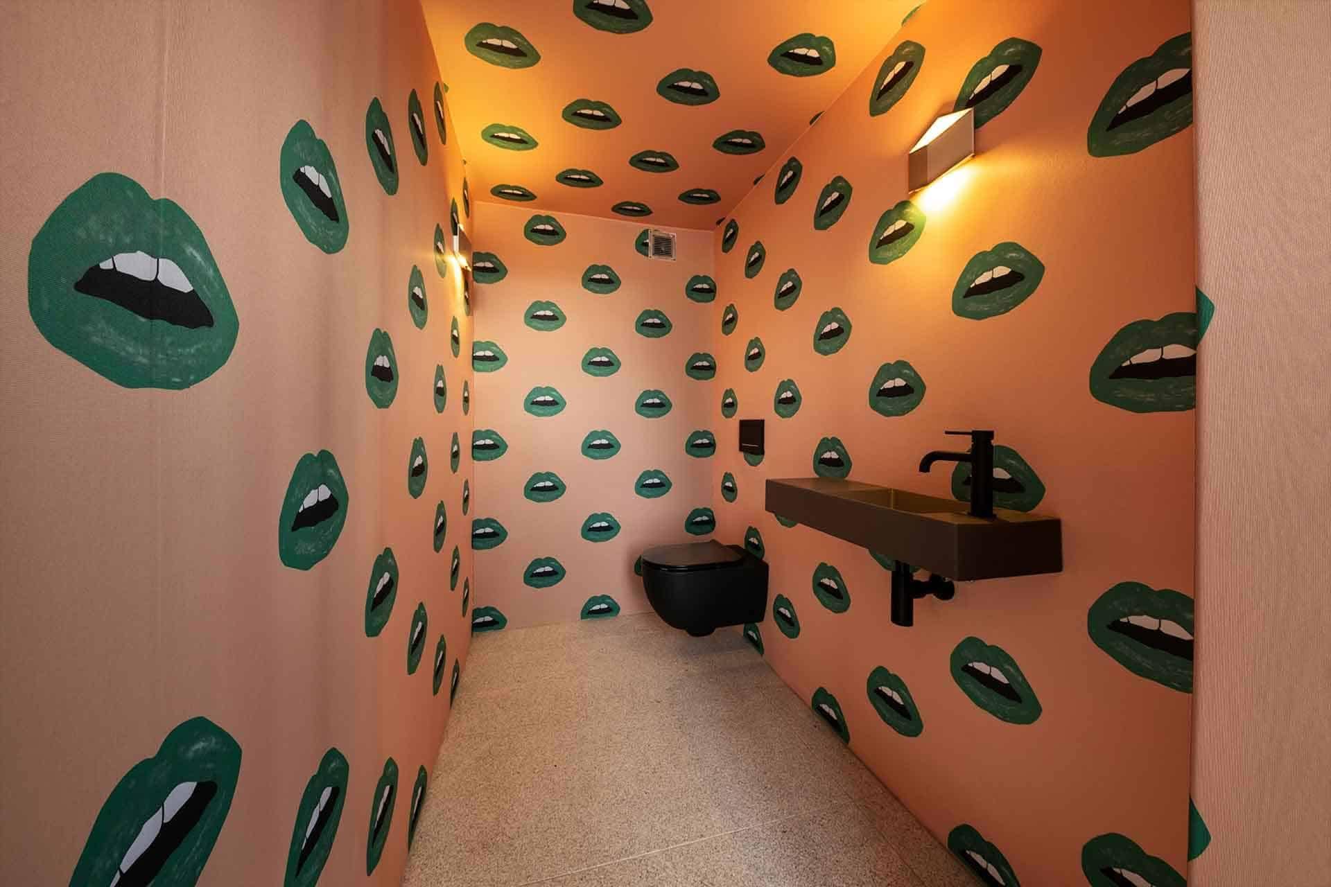 The bathroom from our portfolio showcases walls adorned with patterned wallpaper featuring green lips on a peach background. This eye-catching wallpaper design combines the fresh vibrancy of green lips with the warm, soft tones of peach, creating a distinctive and stylish look in the bathroom.