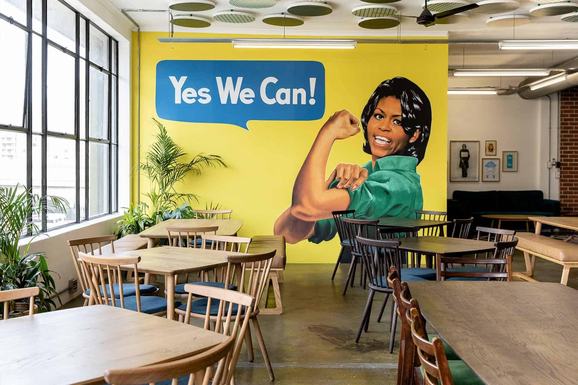 Large, colorful mural featuring a person in a green shirt flexing their arm with the phrase "Yes We Can!" in a blue speech bubble.