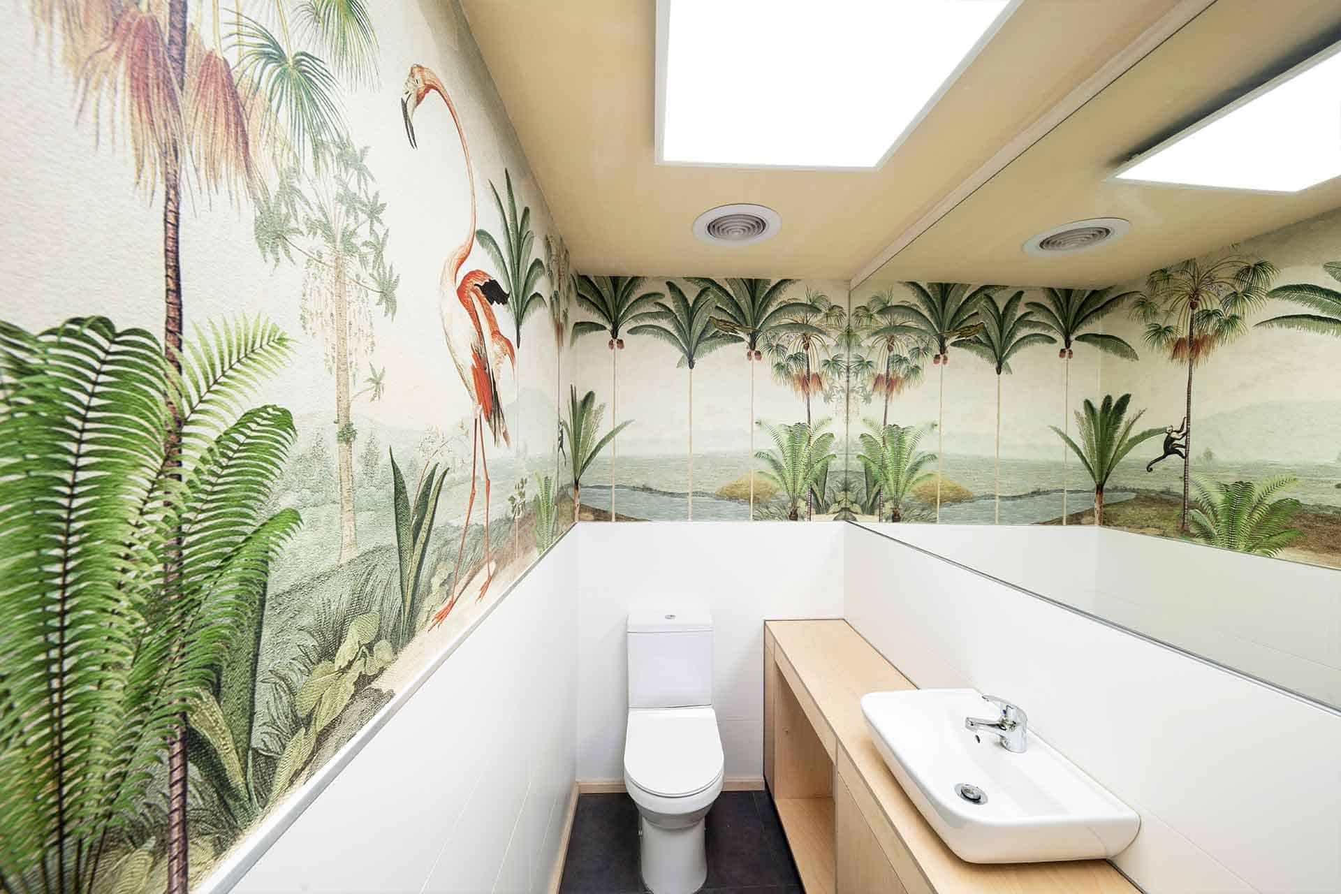 The wallpaper features vibrant murals of flamingos, palm trees, and lush green plants. The colors include vivid pinks (flamingos), rich greens (palm trees and plants), sandy tans, and tropical blues.