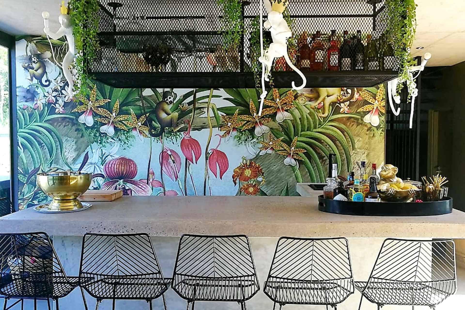Vibrant wall mural featuring an array of lush plants, playful monkeys, and exotic flowers. Colors include rich greens, vibrant reds, deep blues, and sunny yellows. Elements capture jungle foliage and wildlife for a lively atmosphere.