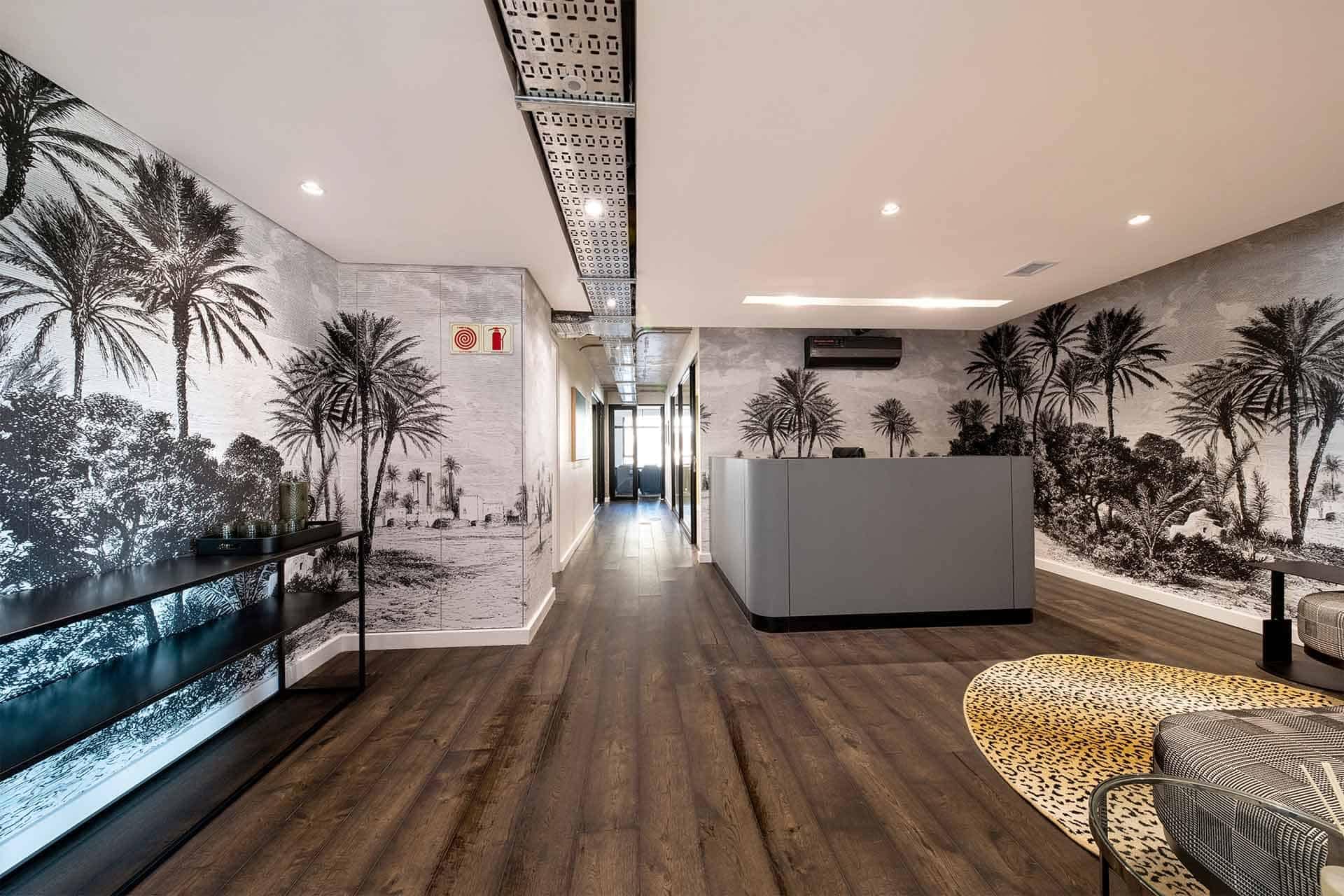 Modern office lobby features tropical wallpaper adorned with vibrant green palm leaves, lush ferns, and exotic flowers in hues of pink and yellow. The background is a subtle off-white, adding depth while letting the greenery pop. This botanical theme creates an inviting atmosphere, blending nature-inspired colors and patterns seamlessly for a fresh yet sophisticated look.