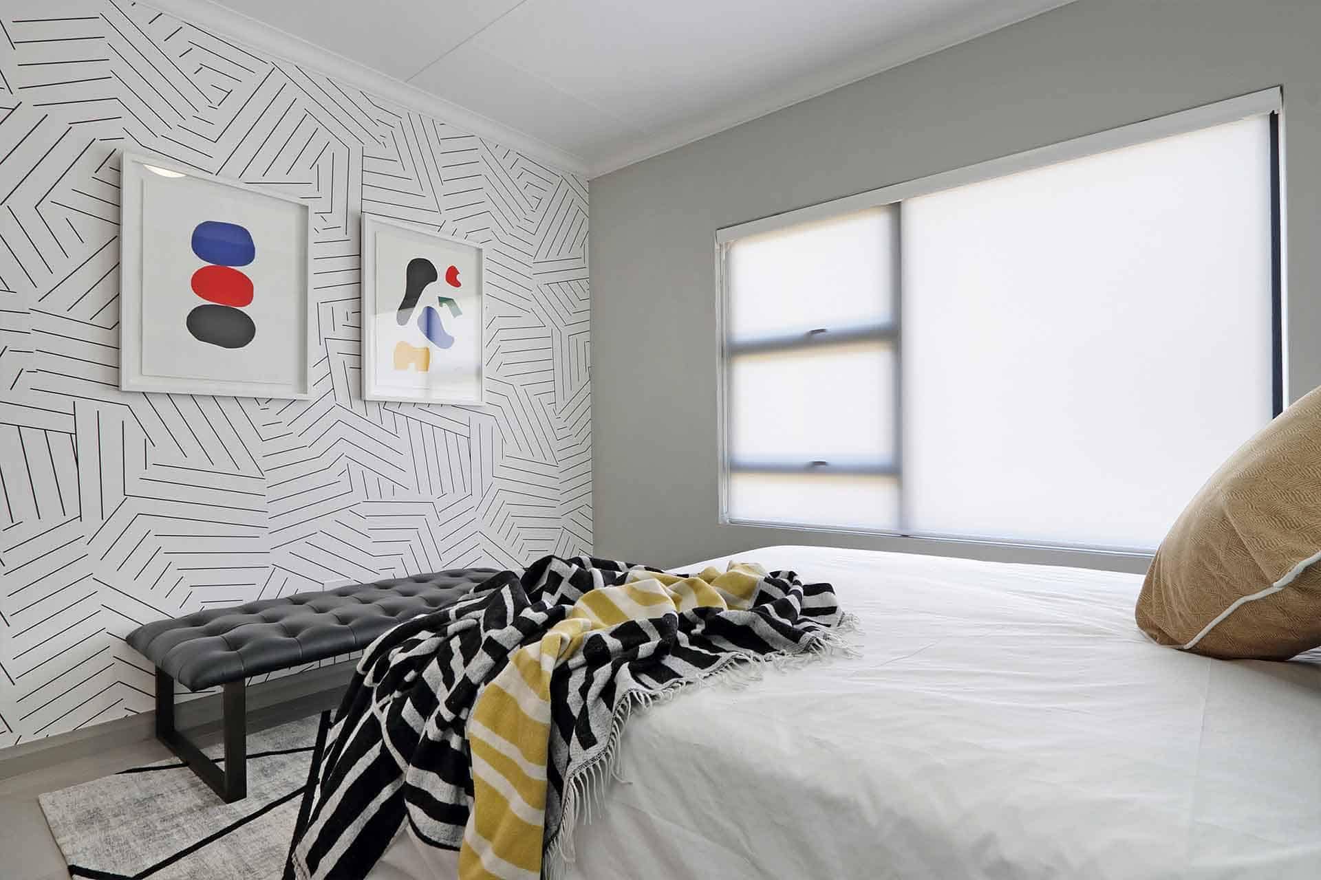 The wallpaper features a geometric pattern with abstract art elements, primarily in shades of gray, white, and subtle accents of muted gold. The design consists of interconnected shapes and lines, creating a visually dynamic backdrop that captures modern aesthetic trends. Ideal for adding depth and sophistication to contemporary bedroom designs.