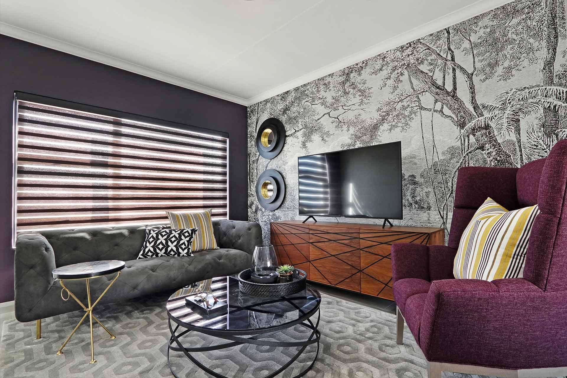 The wallpaper is a black and white nature-themed mural. It features intricate patterns of trees, leaves, and birds, creating a monochromatic and elegant backdrop for the modern living room decor. This statement wall adds depth and visual interest to the space with its detailed illustration of natural elements in contrasting black and white tones.