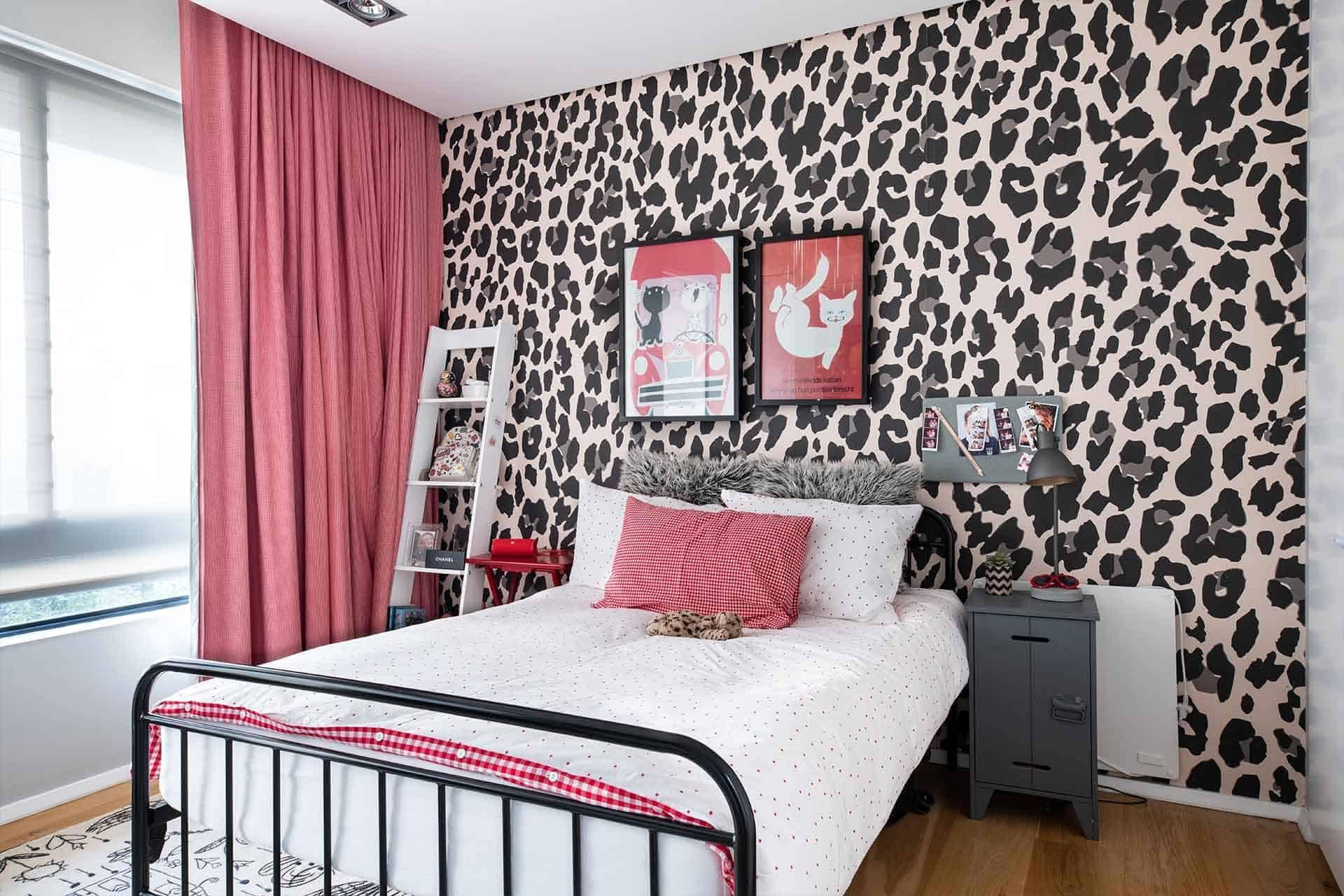 A cozy bedroom showcases an eye-catching leopard print accent wall. The wallpaper features a pattern of bold, contrasting black spots on a warm, golden-brown background. This striking design element adds texture and visual interest to the room, making it perfect for highlighting in your digital portfolio.