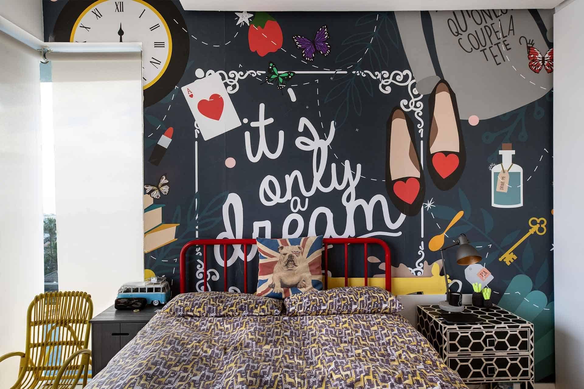 A whimsical mural wallpaper featuring vibrant elements: playing cards, a rabbit, slippers, a potion bottle, and the phrase "It is only a dream." The design is colorful with hues of red, blue, white, and hints of pastel shades. This playful motif serves as the perfect backdrop for creativity and inspiration.