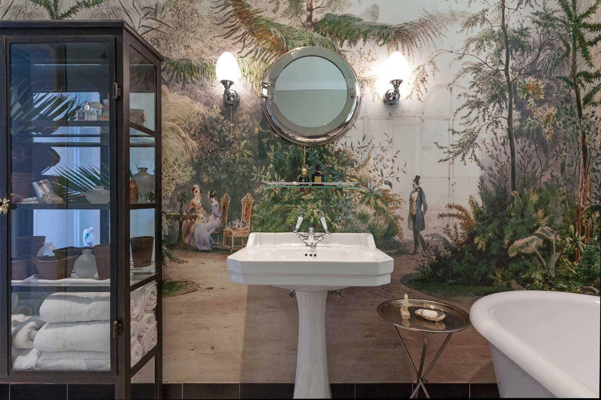 The wallpaper features a detailed mural of an outdoor scene with people and lush greenery. It includes elements like trees, bushes, and figures in period clothing. Dominant colors are green, blue, and earthy tones.