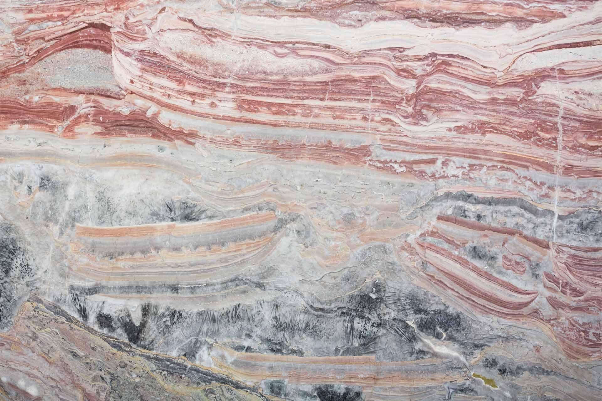 A close-up of a polished stone surface reveals intricate, natural patterns. Shades of red, pink, white, gray, and hints of black create mesmerizing layers and swirls. This abstract painting-like wallpaper varies in complexity by percentage points from each viewing angle.