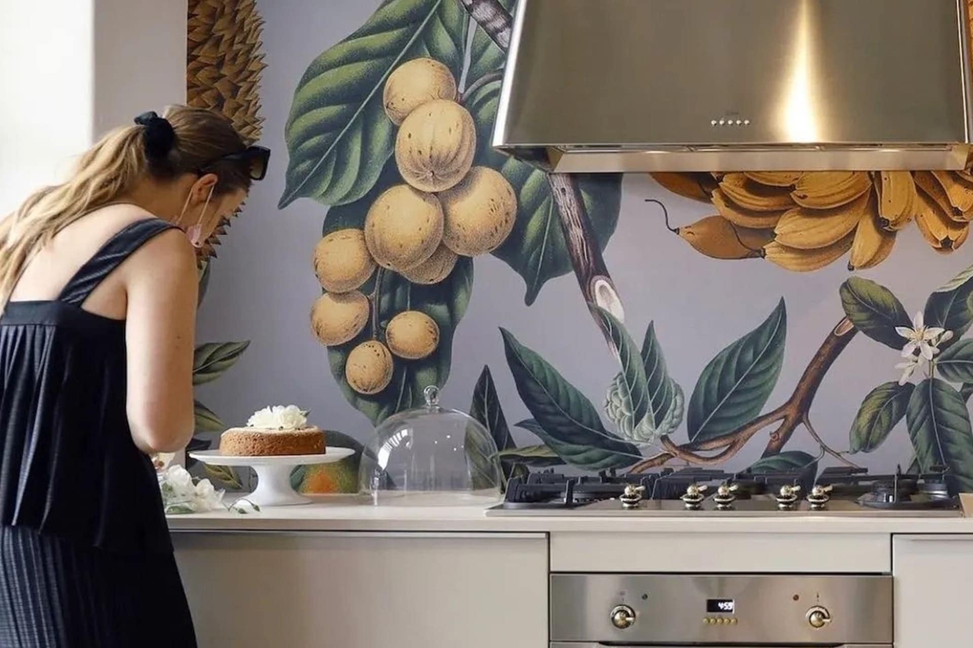 The wallpaper features an array of fruits and greenery, showcasing elements such as oranges, lemons, apples, grapes, and berries interwoven with lush green leaves. The colors include vibrant hues like orange, yellow, red, purple, and various shades of green.