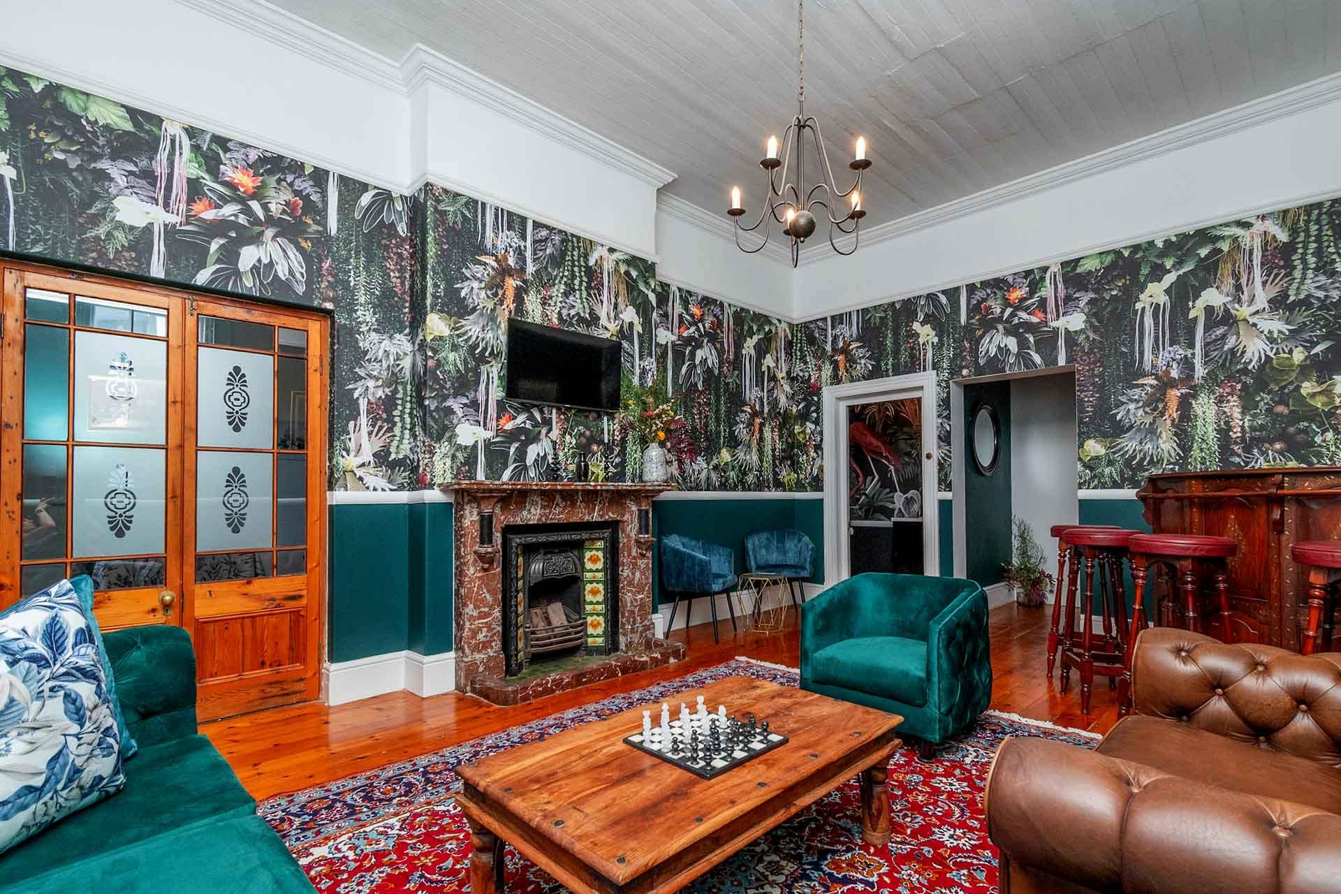 The wallpaper in this stylish living room is a vibrant, jungle-themed masterpiece. It features lush green palm leaves, exotic flowers in bold hues of red and yellow, and playful monkeys swinging from vines. Pops of bright blues and rich earth tones complement the natural greenery, creating a lively and dynamic backdrop that instantly catches the eye. Perfect for showcasing your interior design portfolio.