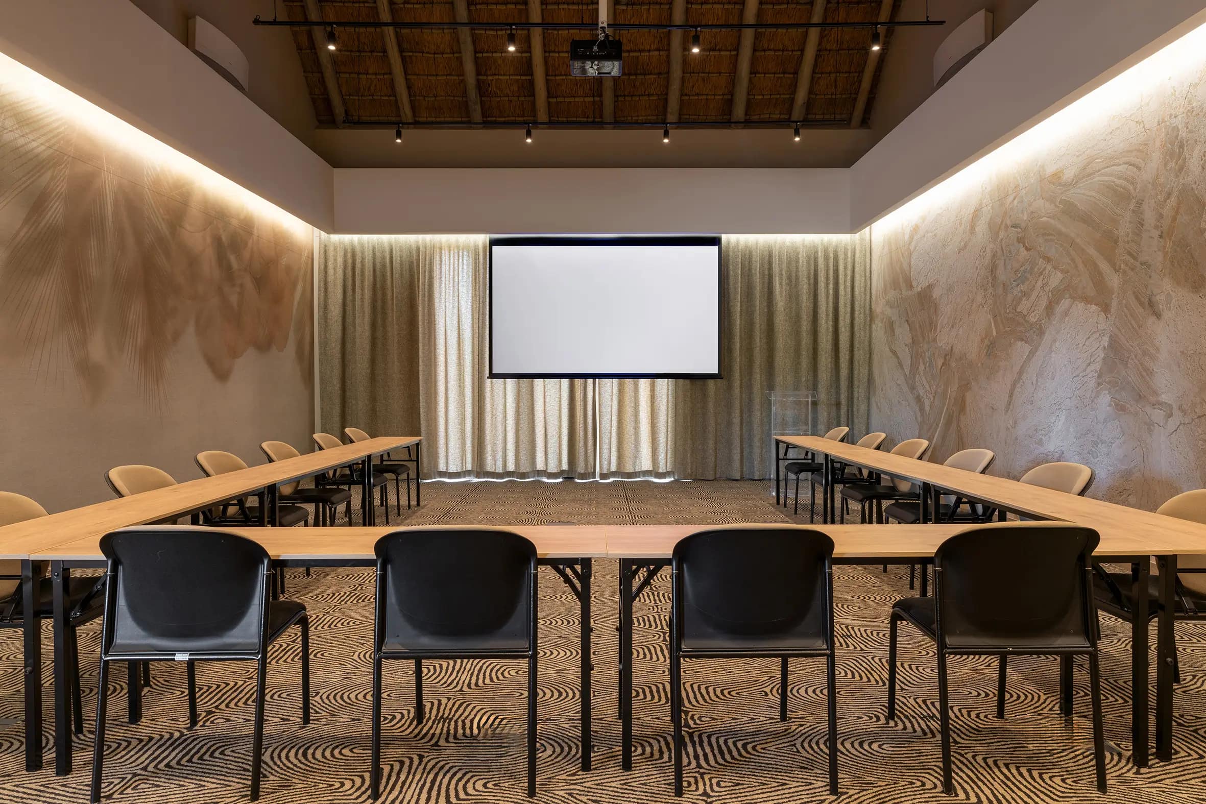The neutral-toned wallpaper in the Radisson Safari Hotel Hoedspruit conference room features subtle patterns in soft beige and taupe, blending seamlessly with the modern decor and providing a sophisticated backdrop to the space.