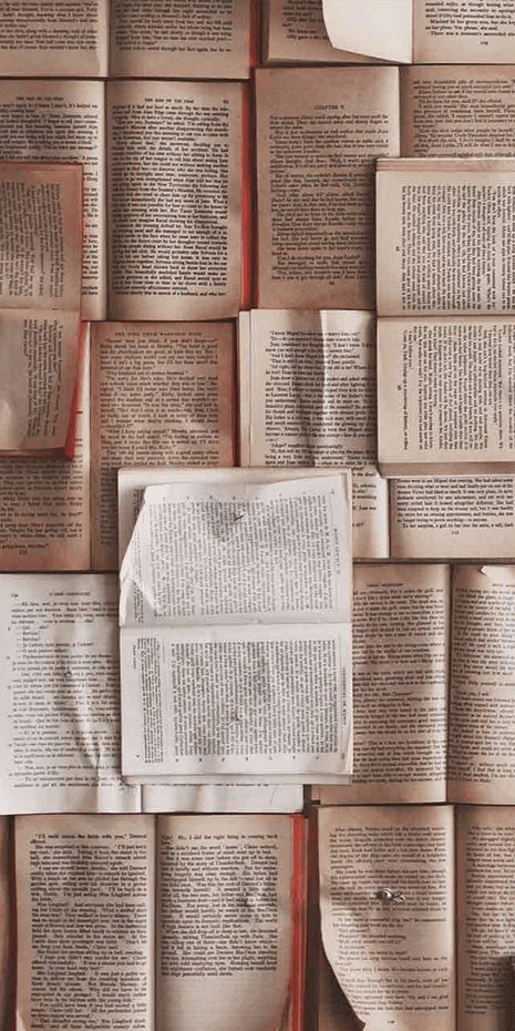 A collage of vintage, open books displays overlapping pages with printed text. The worn edges, slightly crumpled or folded pages enhance a textured look. Predominant elements and colors in the wallpaper include:

- Sepia tones
- Off-white and beige pages
- Black, serif-style printed text
- Faded ink impressions
- Worn edges with slight browning