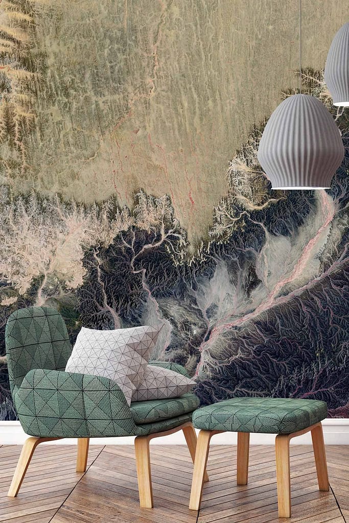 A wall mural featuring intricate patterns akin to landscapes seen from an aerial helicopter tour. The wallpaper showcases a mix of earthy tones, greens, browns, and blues, with detailed lines and curves depicting natural forms like rivers and fields. Intricacies include delicate textures resembling mountain ranges and valleys in subdued shades to complement the cozy setting.