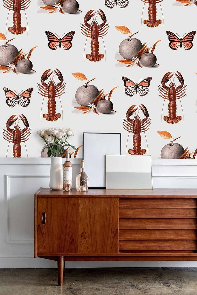 The whimsical Nineteen Eighty wallpaper features illustrations of lobsters, butterflies, oranges, and autumn leaves. The design incorporates vibrant colors including reds (lobsters), blues and yellows (butterflies), oranges (fruits), and various shades of browns and reds (autumn leaves).