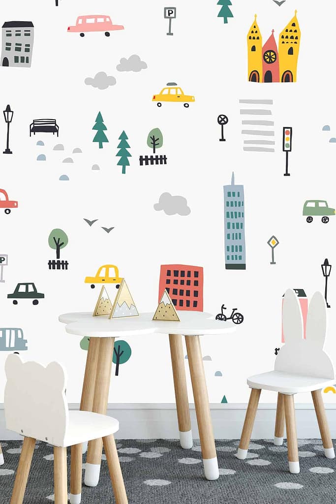 The wallpaper features playful city-themed illustrations with vibrant cars, tall buildings, green trees, and fluffy white clouds. The colors include varied shades of blue for the sky and buildings, bright red and yellow for the cars, and lush green for the trees.
