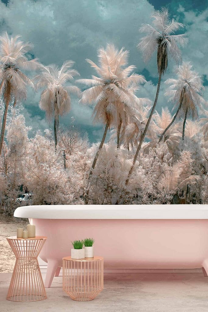 Surreal landscape wallpaper featuring a pastel pink bathtub, tall light pink palm trees, a cloudy teal-colored sky, subtropical elements with small matching tables, candles, and plants for a whimsical and dreamy outdoor bathroom setting.