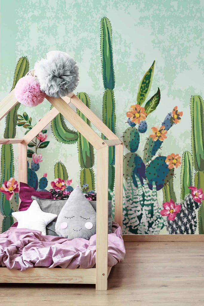 A vibrant mural featuring various cacti and colorful flowers, with hues of green, pink, yellow, and blue. Cacti include tall saguaros, round barrel cacti, and paddled prickly pears. Flowers are vividly represented with colors like bright reds, soft pinks, sunny yellows, soothing blues, and deep purples. The mural creates a lively and whimsical atmosphere in the nursery child's bedroom.