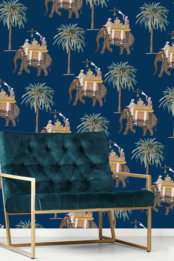 Dark blue wallpaper with a repeating pattern of elephants in procession. Elephants are adorned with riders and palm trees. Colors include rich golds, deep blues, greens, and hints of red. Exotic, vintage design inspired by traditional Indian motifs and grand wedding celebrations.