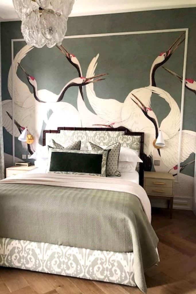 A bedroom featuring a bird-themed mural highlighting white cranes with red crowns on the wall behind the bed. The wallpaper showcases elegant cranes in flight, creating a serene atmosphere with its detailed depiction of these majestic birds. The combination of white and red on the cranes adds a striking contrast against possibly muted or natural background tones, making it an eye-catching focal point in the room.