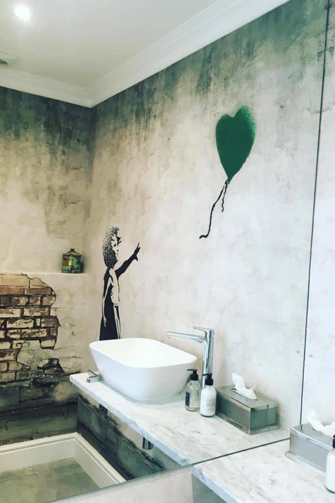 Wallpaper featuring a mural of a child reaching for a green heart-shaped balloon. Includes elements like detailed faux bricks for a rustic touch. Predominant colors: green, white, gray, and rustic red from the faux brickwork.