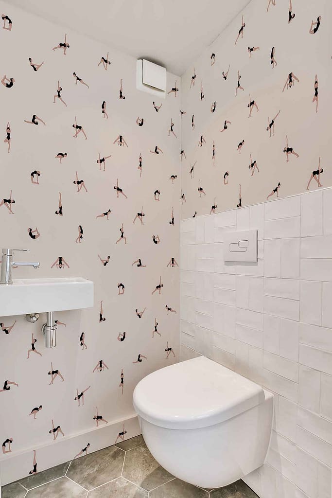 A modern bathroom featuring unique wallpaper with small, repeated illustrations of people in various poses. The design adds life with vibrant colors including shades of blue, red, yellow, and green against a light background. This playful and dynamic wallpaper serves as the focal point of the space.
