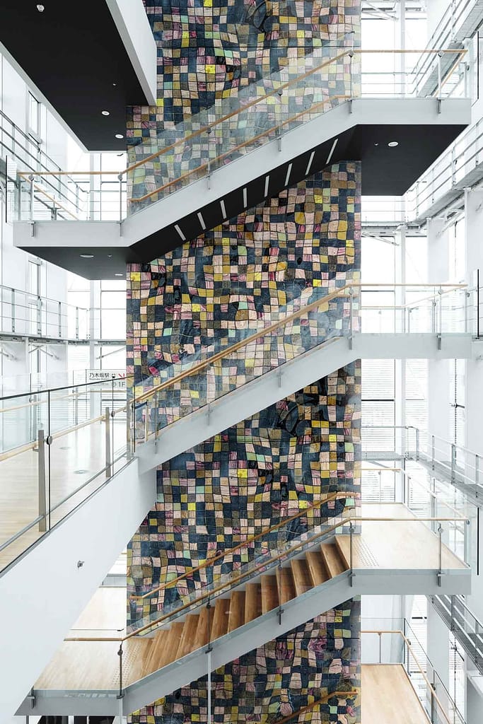 The wallpaper features a colorful, mosaic-like pattern made of small, rectangular tiles. Elements include vibrant hues such as deep blues, rich reds, lush greens, and bright yellows. The artistic design adds a dynamic and contemporary touch to the sleek interior.